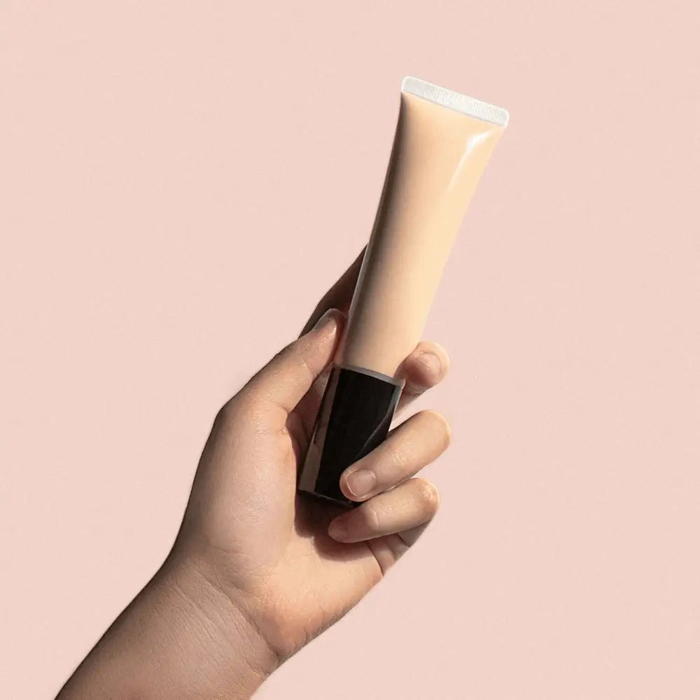 Person holding MIANIMED premium skincare cream tube against a light pink background.